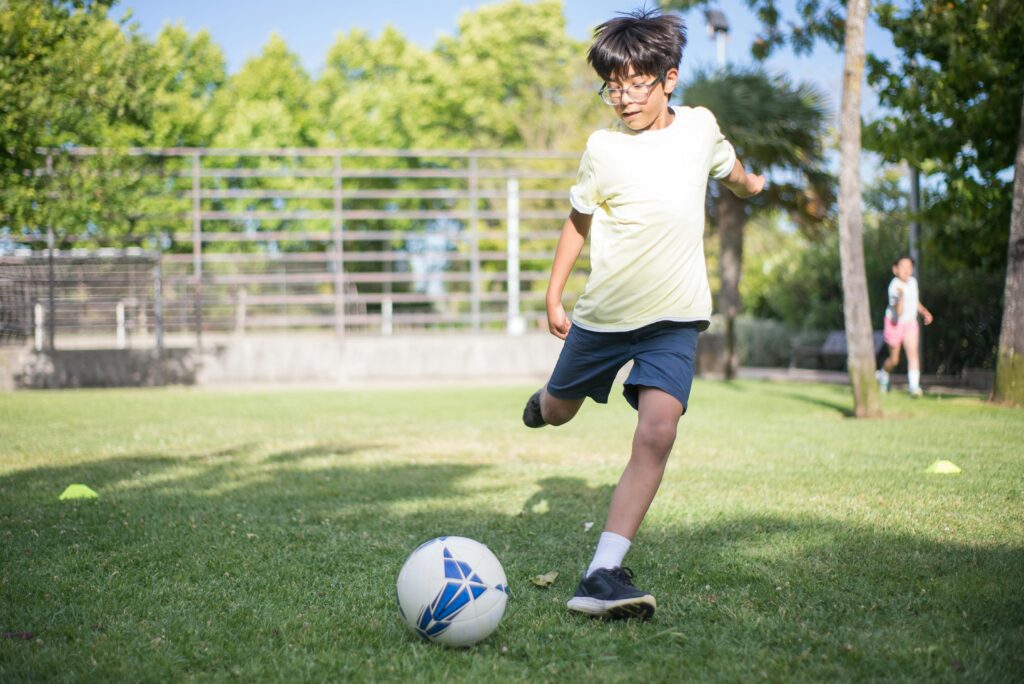 Young boy kicking a soccer ball on a grassy field during a sunny day. Perfect for sports and outdoor play themes.